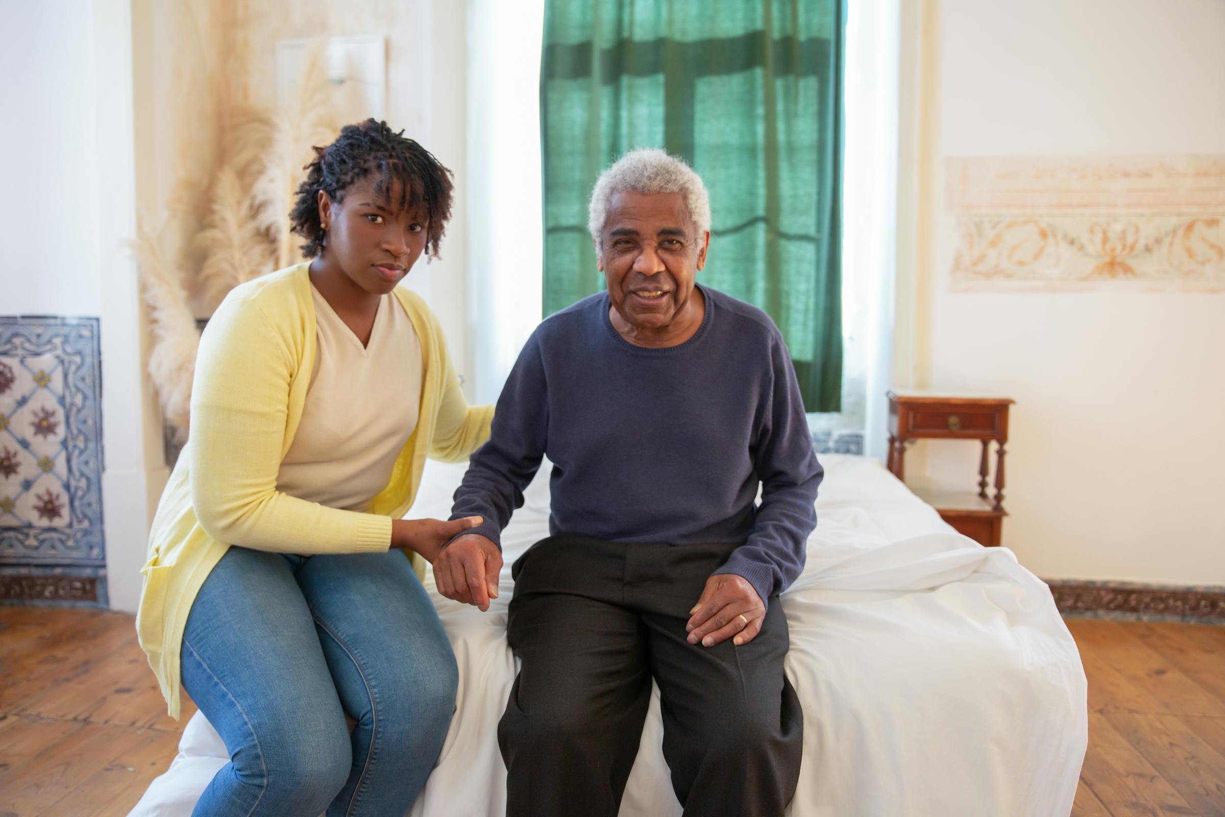 A support worker holding hands with an older man, sitting together at home