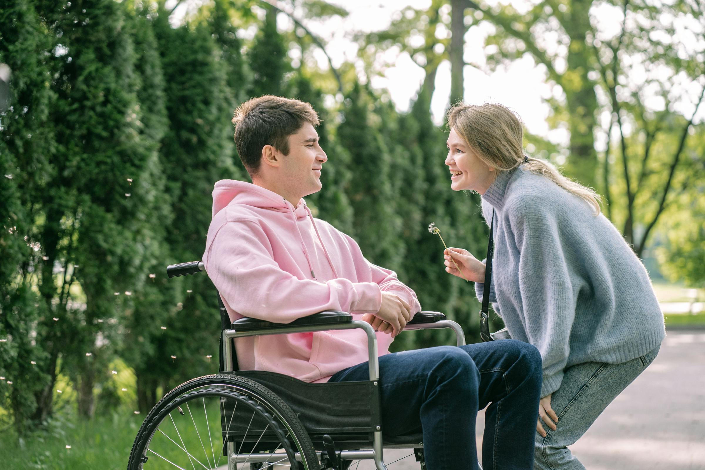 A support worker and a young man who uses a wheelchair smiling together outdoors
